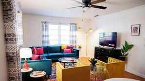 Ein Wohnzimmer mit einem blauen Sofa, einem gelben Sessel, einem Couchtisch, einem Fernseher und einem Deckenventilator.