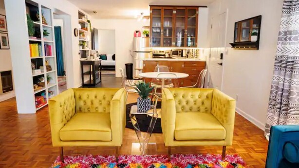 Ein Wohnzimmer mit einem gelben Sofagarnitur, einem Couchtisch und einem farbenfrohen Teppich.