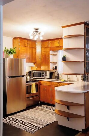 A compact kitchen with wooden cabinets, stainless steel appliances, and a white countertop.