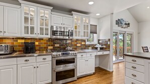 A modern kitchen with white cabinetry, stainless steel appliances, and a herringbone tile backsplash.