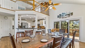 A spacious dining area with a wooden table set for six, surrounded by chairs. A staircase with a wooden railing leads to an upper level.