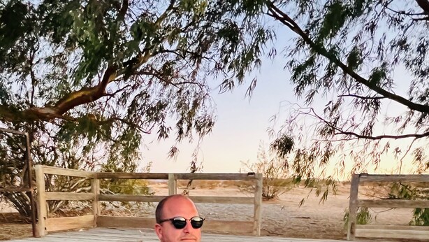 A person relaxing in a wooden deck with a pool, surrounded by trees and a fence. - Joshua Tree Hot Springs House (Twentynine Palms)
