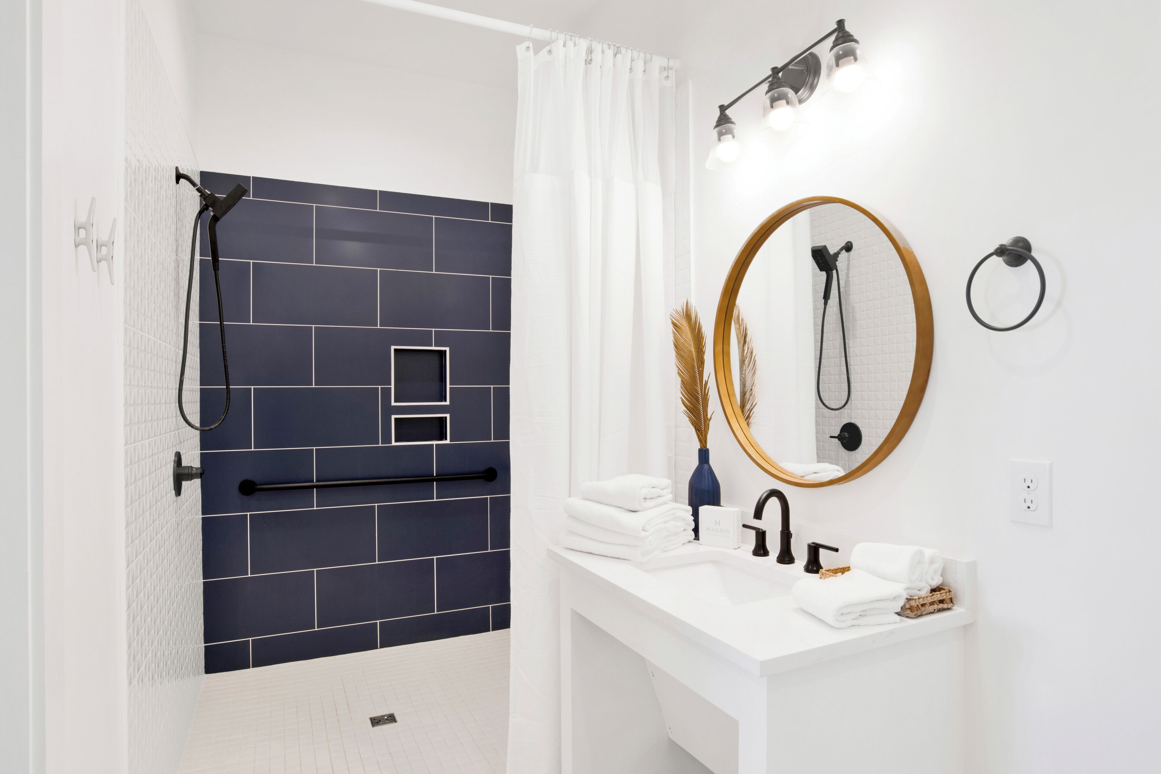 Een moderne badkamer met een douche, een witte wastafel, een spiegel en een handdoekrek.