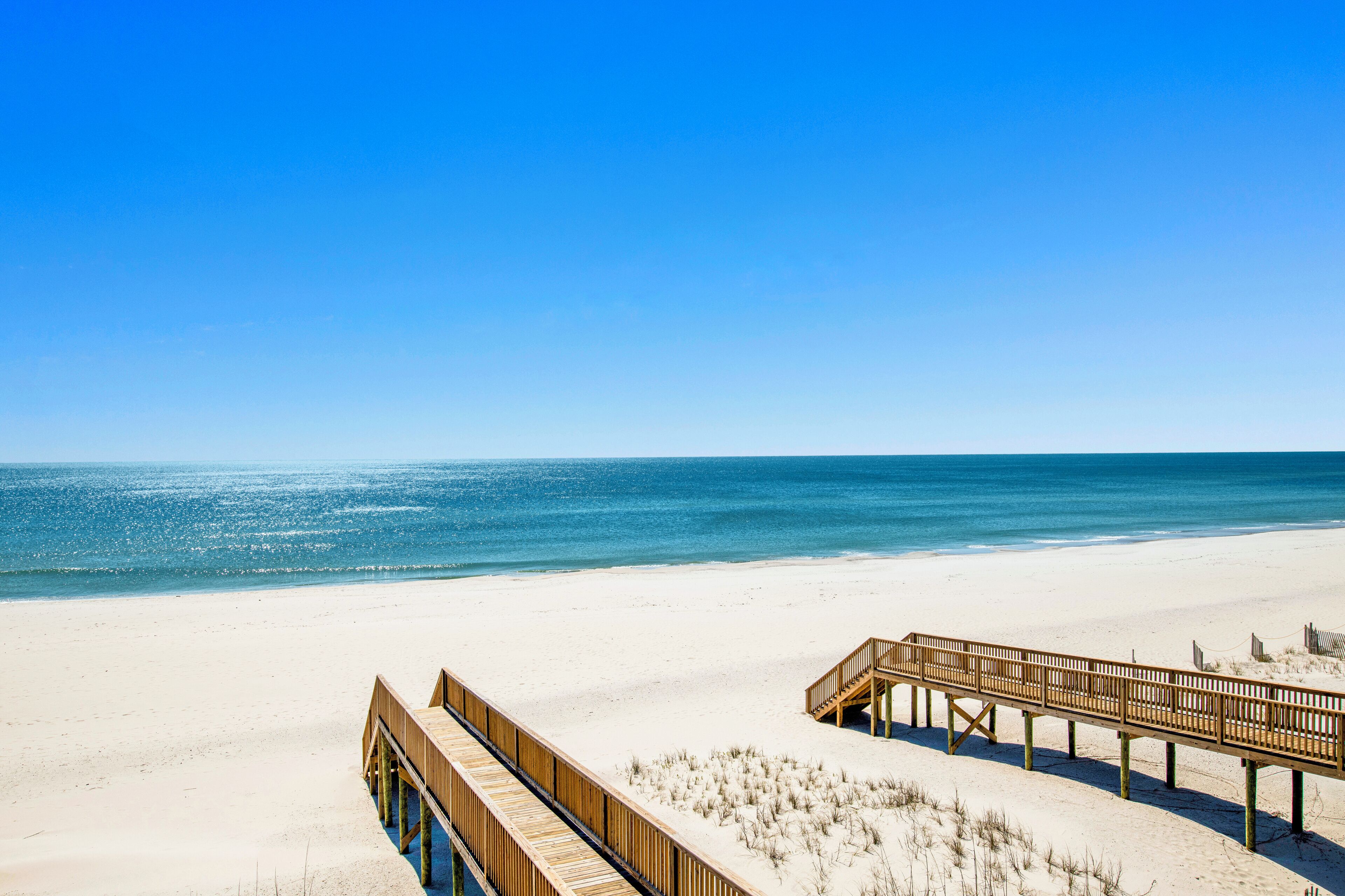 A beach with a wooden boardwalk leading to a pier.