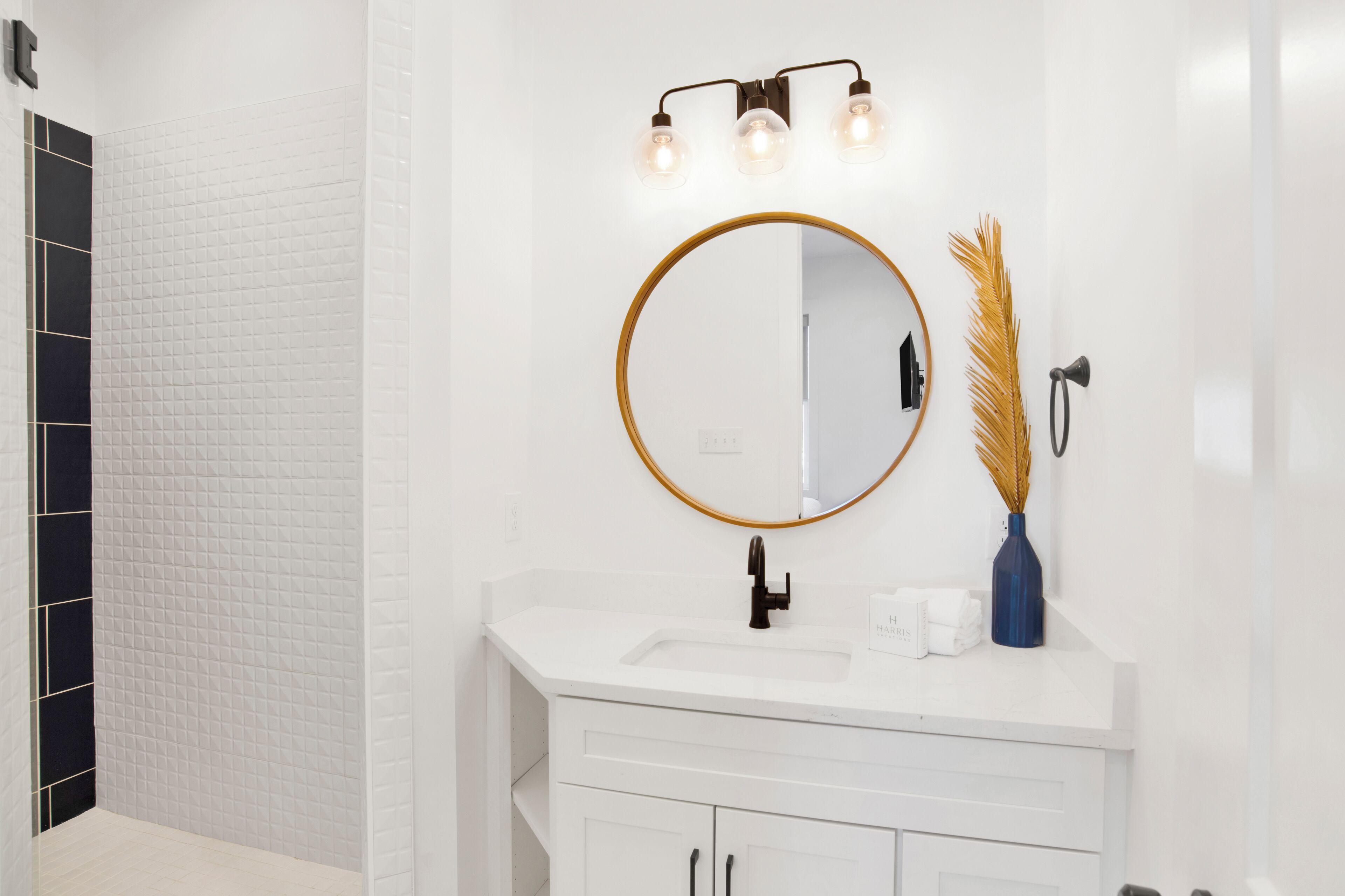 Une salle de bain avec un lavabo blanc, un miroir rond doté d’un cadre doré et un luminaire fixé au mur.
