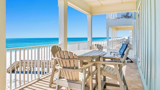 A covered outdoor area with a view of the beach, wooden chairs, and a table.