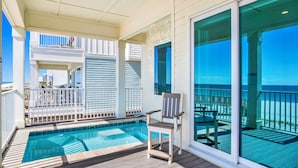A balcony with a pool, a chair, and a view of the ocean.