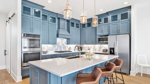 A modern kitchen with blue cabinets, stainless steel appliances, and a central island with bar stools. - Beachfront Luxury | Private Pool | Elevator | Pet Friendly (Gulf Shores)
