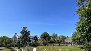 A grassy outdoor area with Adirondack chairs and a wooden deck. - Charming Historic Downtown Cottage (Nantucket)