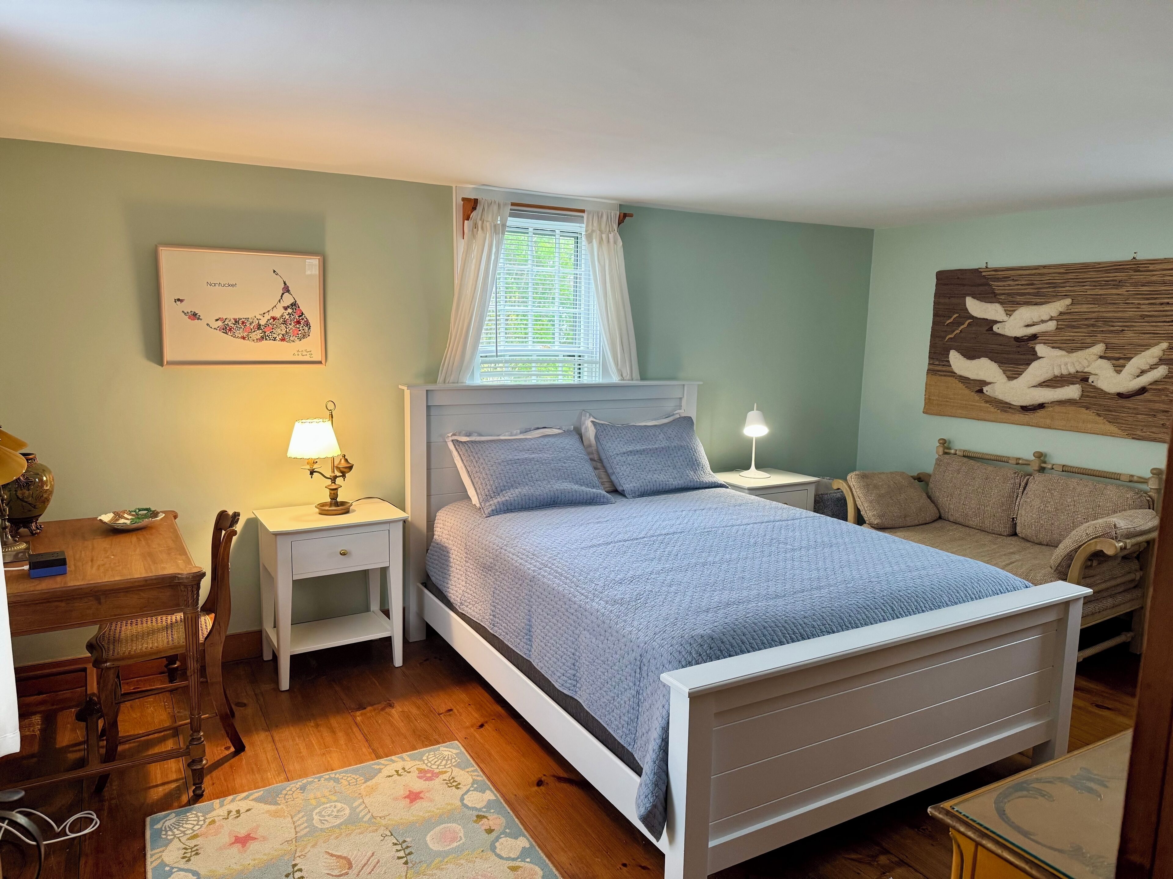 Une chambre à coucher comprenant un lit, des tables de chevet, un bureau, une chaise, un tapis et des œuvres d’art accrochées aux murs.