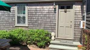A house with a grey shingle exterior, a white door with a small window, and a green umbrella. - Charming Historic Downtown Cottage (Nantucket)