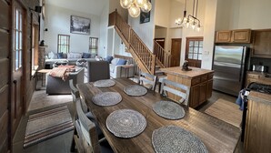 Amplia sala de estar con mesa de comedor de madera, cocina con refrigerador de acero inoxidable y escalera que conduce a un nivel superior.