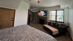 Un dormitorio con cama, ventilador de techo, chimenea, televisor y ventana con persianas.