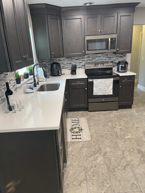 A modern kitchen with dark cabinetry, a stainless steel sink, a microwave, and a stove.
