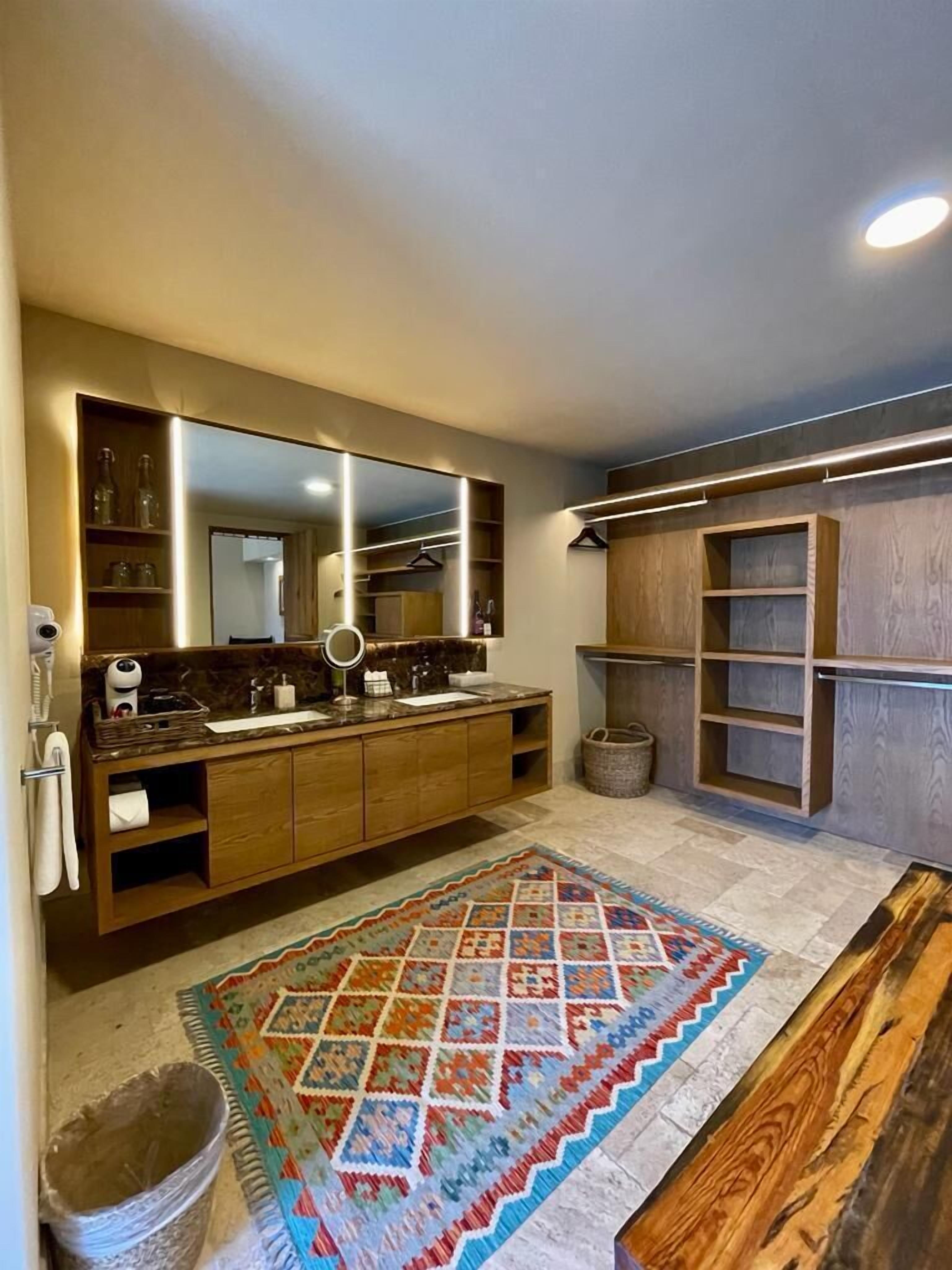 Une salle de bain moderne avec un grand miroir, un meuble-lavabo en bois et un tapis coloré.