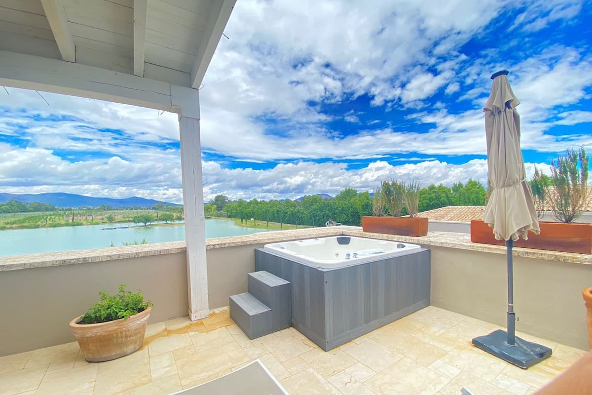 A rooftop terrace with a hot tub, potted plants, and a view of a lake and mountains.