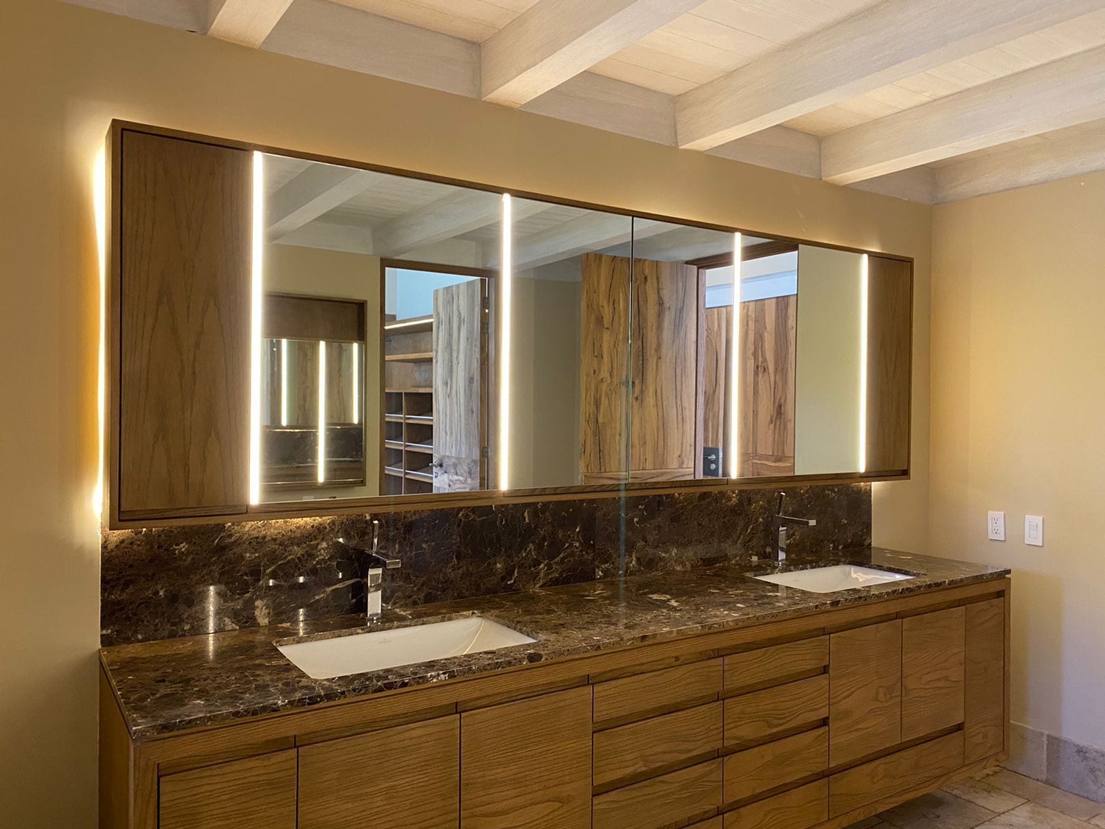 A bathroom with a large mirror, two sinks, and wooden cabinetry.