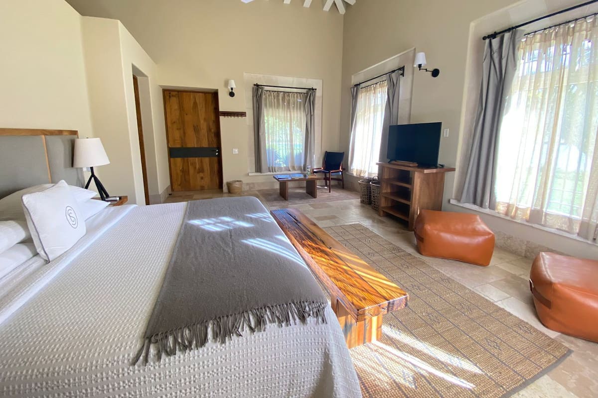 A hotel room with a large bed, a wooden bench, a TV, and a window with curtains.