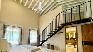 A spacious bedroom with a large bed, a wooden headboard, a staircase, and a view into the kitchen area. - HOTEL VIÑEDOS SANTA CATALINA (San Miguel de Allende)