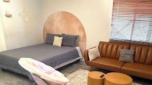 Quarto moderno com uma cama, um sofá, uma cadeira e duas mesinhas de cabeceira de madeira.