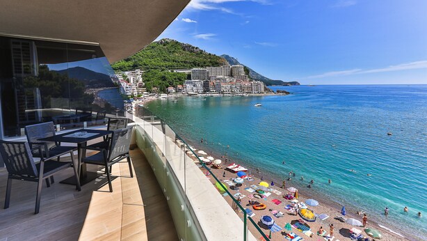 Un balcón con vista a una playa, un comedor y una montaña al fondo.