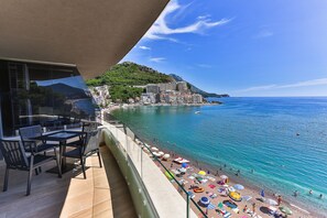 A balcony with a view of a beach, a dining area, and a mountain in the background. - Palacio Del Mar (Rafajlovici)