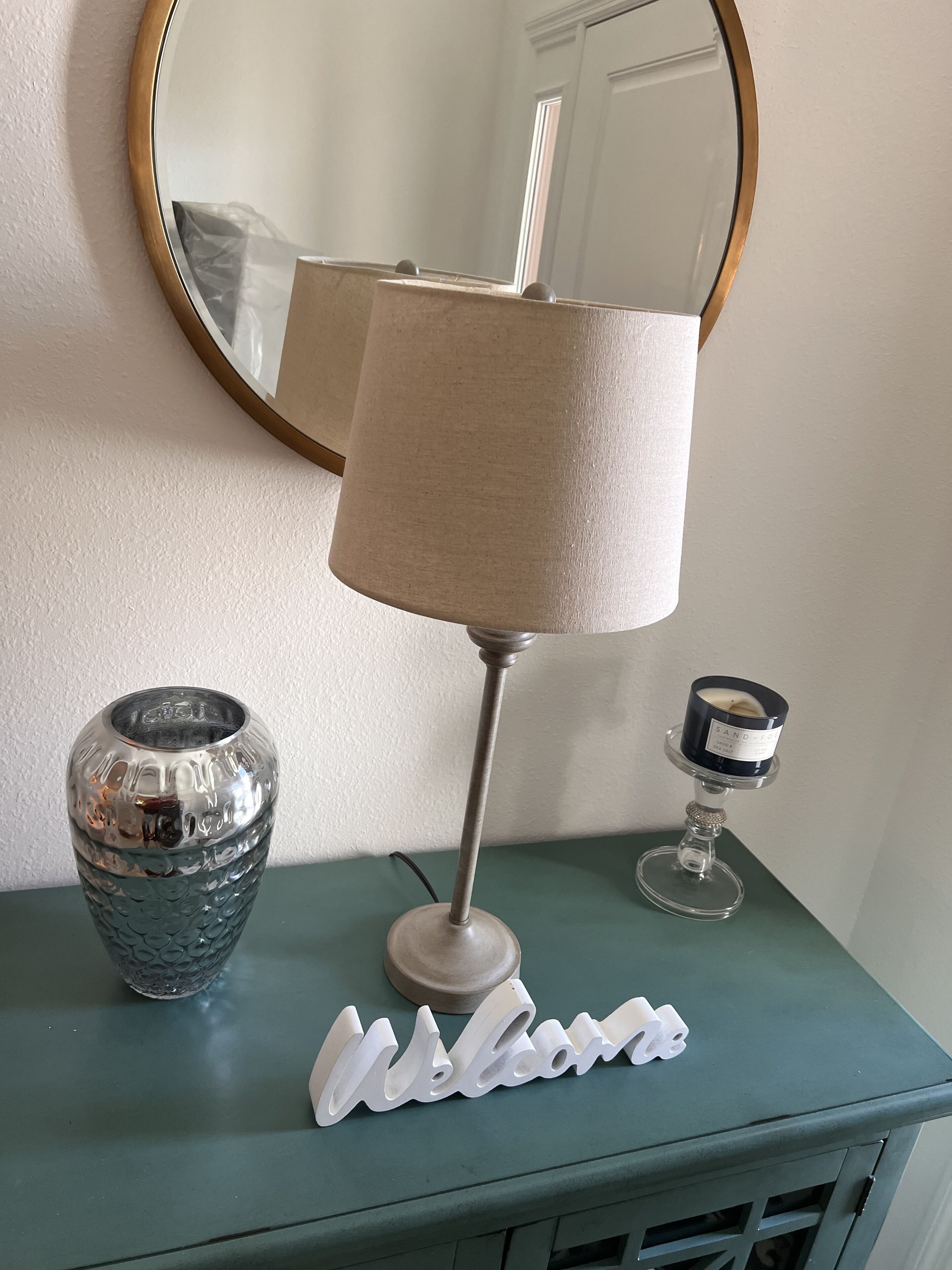 A green console table with a lamp, a decorative vase, and a candle holder.