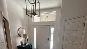 A hallway with a white door, a black console table with a lamp, a mirror, and a patterned rug. - Ultra clean designer home in The Villages (3-bed) (Wildwood)