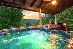 Ein Whirlpool mit Blick auf Berge und Bäume, eine amerikanische Flagge sowie eine Holzterrasse mit Tisch und Stühlen.