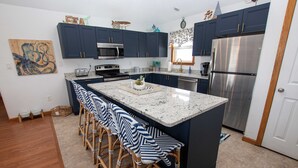 A modern kitchen with dark blue cabinets, stainless steel appliances, and a central island with bar stools. - Oceanside, Private Pool, Close to the beach! OS1F, La Maison de la Mer (Corolla)