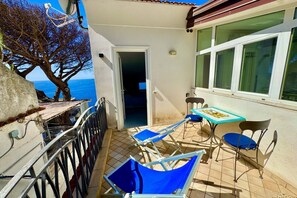 Un balcon avec vue sur la mer, une table avec des chaises et une porte donnant sur lâintĂ©rieur.