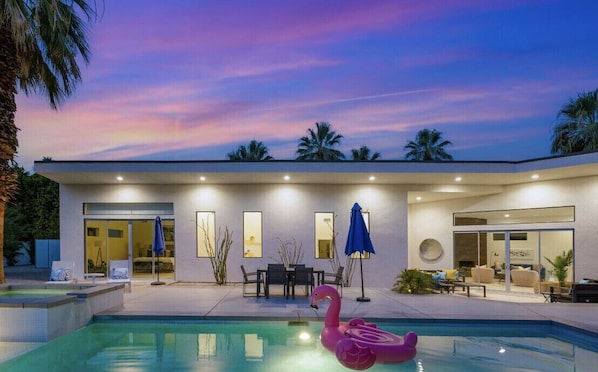 A modern house with a swimming pool, outdoor furniture, and a flamingo float.