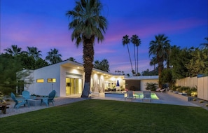A modern house with a pool, outdoor seating, and palm trees.