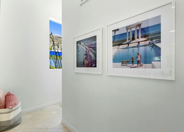 A hallway with two framed pictures on the wall, a pet bed, and a window with a view of a mountain and a blue sky.