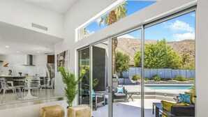 Una cocina moderna con comedor, un amplio ventanal corredera que da a una piscina con mobiliario exterior.