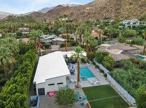 A modern house with a swimming pool, surrounded by palm trees and a mountain backdrop.