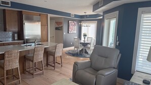 A modern kitchen with a stainless steel refrigerator, wooden cabinets, and a dining area with wicker chairs and a table.