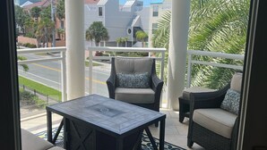 A balcony with wicker furniture, a ceiling fan, and a view of the street and buildings.