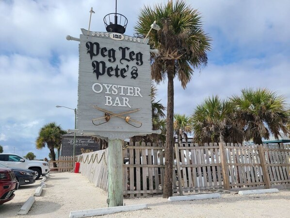 A wooden sign for Peg Leg Pete's Oyster Bar with a beach view.