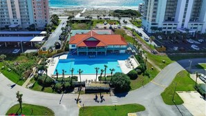 A hotel with a large pool, surrounded by palm trees and a view of the ocean.