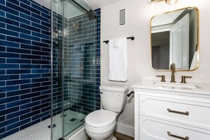 Un baño con ducha acristalada, inodoro blanco y tocador con espejo y lavabo.