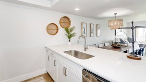 A modern kitchen with white cabinetry, a stainless steel sink, and a hanging light fixture.