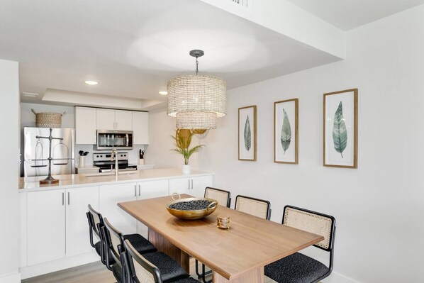 Una cocina moderna con armarios blancos, una mesa de comedor de madera y una lámpara colgante.