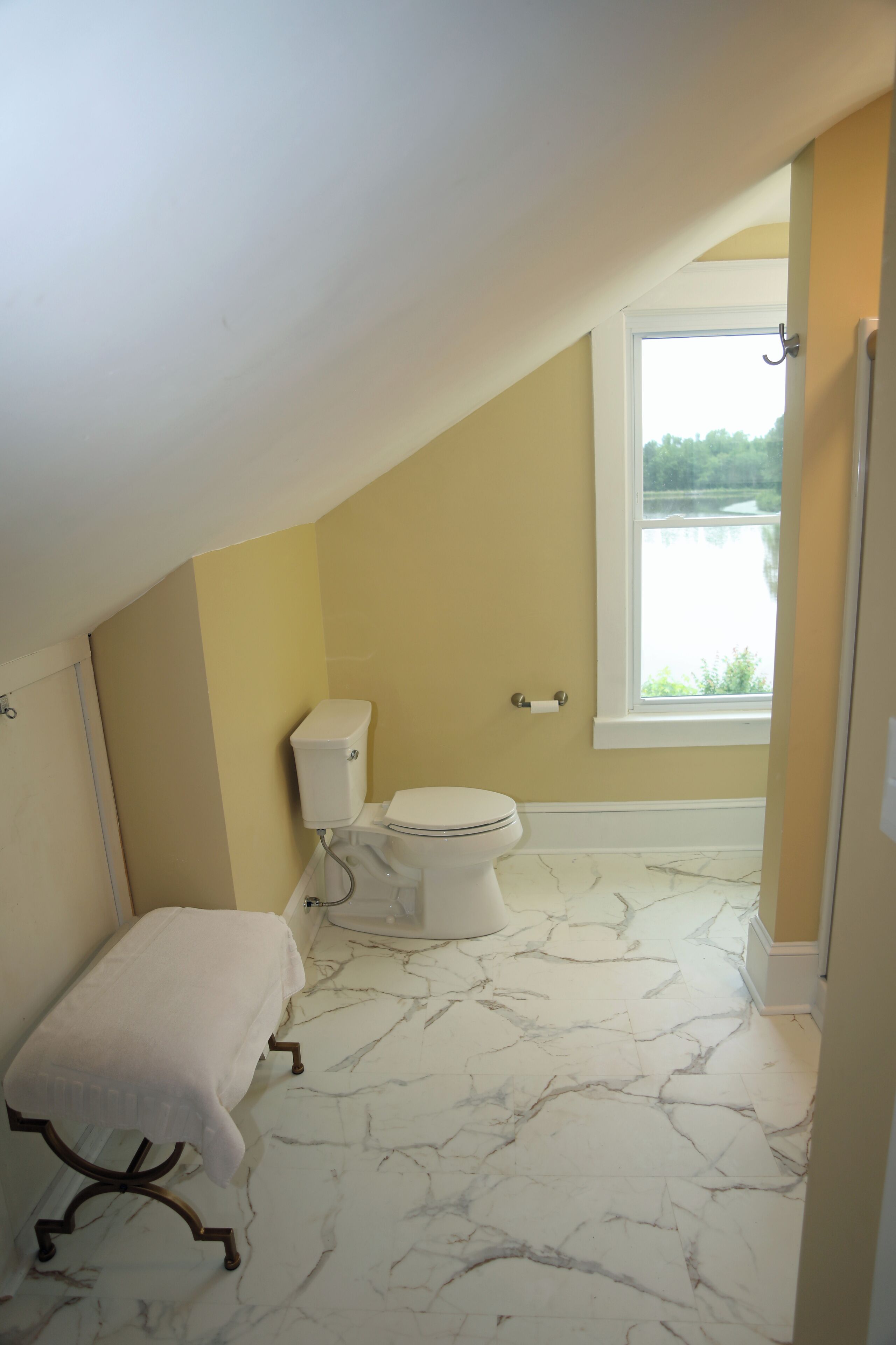 Ein kleines Badezimmer mit Toilette, Sitzbank und Fenster.