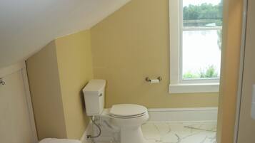Ein kleines Badezimmer mit Toilette, Sitzbank und Fenster.