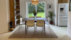 A dining area with a table, chairs, a woven pendant light, a bookshelf, a refrigerator, and a view of the outdoors. - Spacious house in serene peaceful setting 15 min from Lake Crescent&Crescent Bch (Port Angeles)