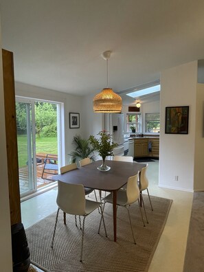 Une cuisine moderne dotée d’un grand îlot central, d’un coin repas avec une table ronde et des chaises, et offrant une vue sur un jardin luxuriant grâce à de grandes portes-fenêtres coulissantes.
