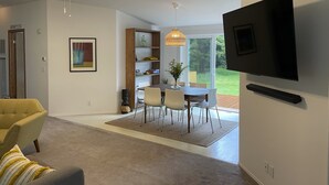 A modern living room with a flat-screen TV mounted on the wall, a dining area with a table and chairs, and a ceiling fan. - Spacious house in serene peaceful setting 15 min from Lake Crescent&Crescent Bch (Port Angeles)