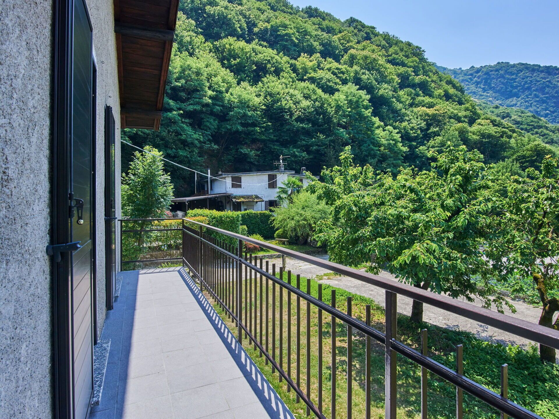 A balcony with a view of a lush green hillside and a house in the background.