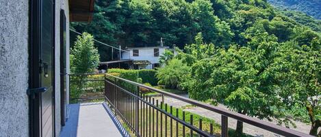 A balcony with a view of a lush green hillside and a house in the background.